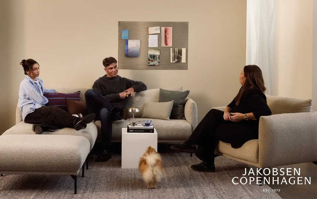 Drei Personen auf hellem Sofa mit Hocker und kleinem Hund auf Teppich im Wohnzimmer